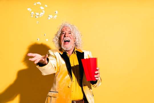 Cheerful senior man catching popcorn against yellow background
