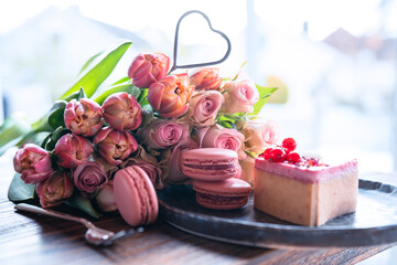 Beautiful bouquet of flowers with sweet delicacies. Heart shape, sweet pastries with pink roses and tulips on wooden table. Background for mother's day and weddin