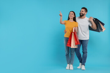 Happy couple with shopping bags looking at something on light blue background. Space for text