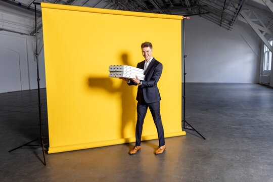 Businessman holding pizza boxes stack in front of yellow backdrop