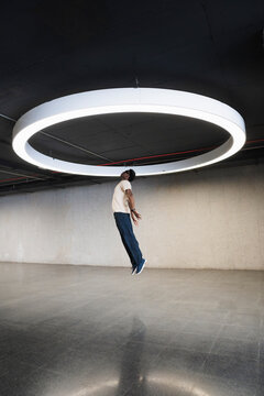 Young man with futuristic cyber glasses jumping under modern ring lamp