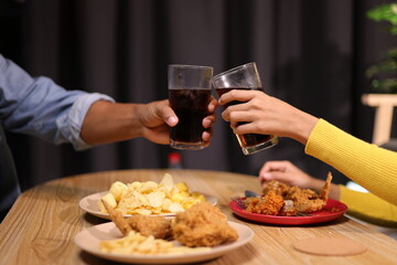 Young man and woman are eating dinner together at home. Friends eating fried chicken, drinks and snacks together while having dinner at home.