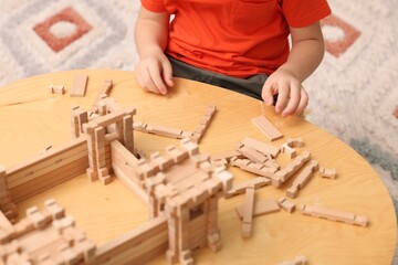 Little boy playing with wooden construction set at table in room, closeup. Child's toy