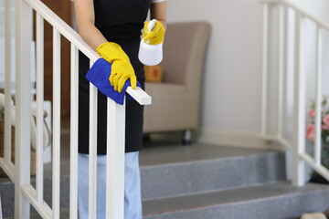 A female cleaner is using a cloth to clean the stair railings in the house.