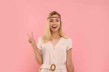 Portrait of happy hippie woman showing peace sign on pink background