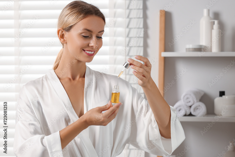 Wall mural Beautiful woman with cosmetic serum in her hands in bathroom