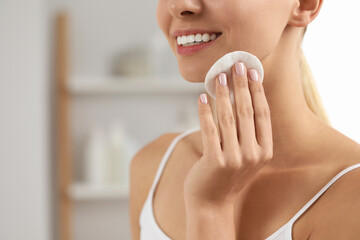 Smiling woman removing makeup with cotton pad indoors, closeup. Space for text