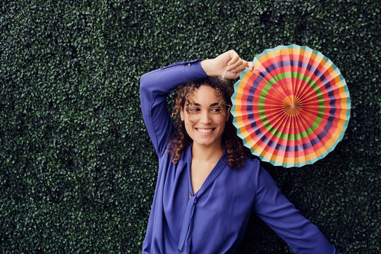Happy businesswoman holding colorful folding fan in front of hedge