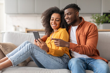 Cheerful black young couple having fun with cellphone at home