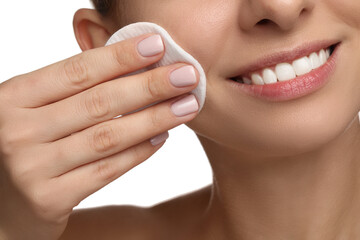 Smiling woman removing makeup with cotton pad on white background, closeup
