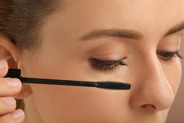 Woman applying mascara onto eyelashes, closeup view