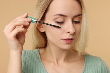 Beautiful woman applying mascara on beige background, closeup