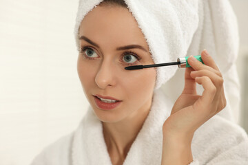 Beautiful woman applying mascara with brush indoors, closeup