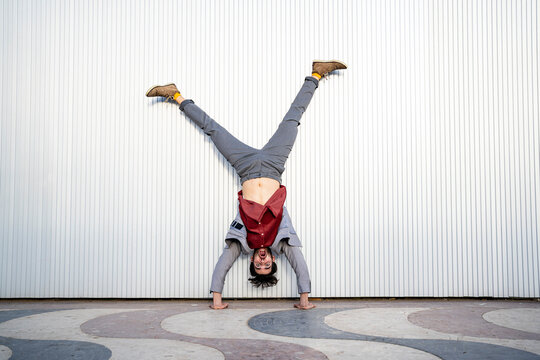 Businessman doing handstand on footpath in front of wall