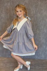 happy blonde girl with pigtails in a gray school dress on a gray background
