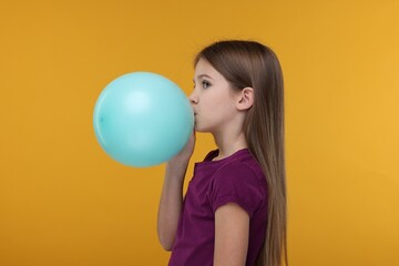 Girl inflating bright balloon on orange background