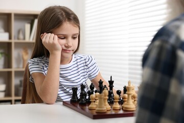 Girl playing chess with her grandfather at table in room