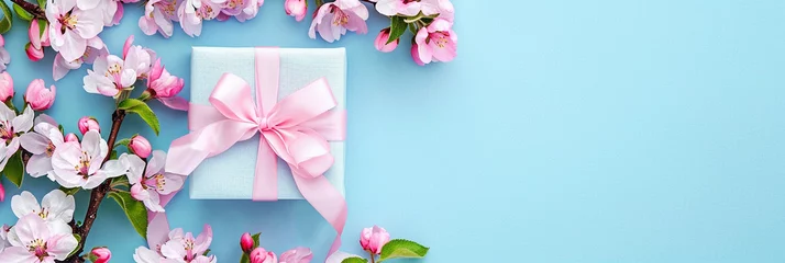 Fotobehang Gift box with pink ribbon and spring cherry blossoms on a blue background. Layout, top view. Banner, card, cover with place for text © Irina