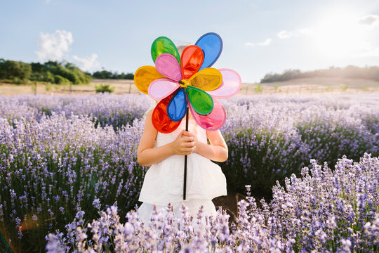 Girl in white dress covering face with pinwheel toy on sunny day