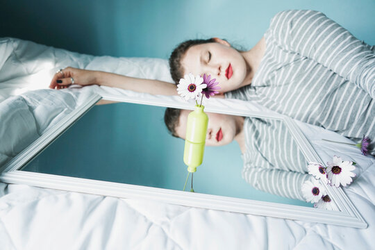 Young woman sleeping next to mirror lying on white duvet