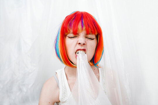 Angry woman with multi colored dyed hair biting plastic