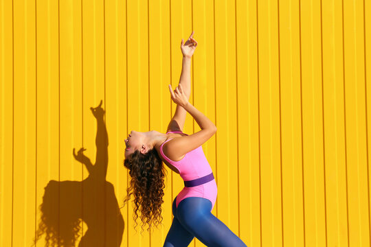Young woman wearing bodysuit dancing in front of yellow wall