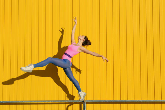 Carefree woman practicing ballet on railing in front of yellow wall