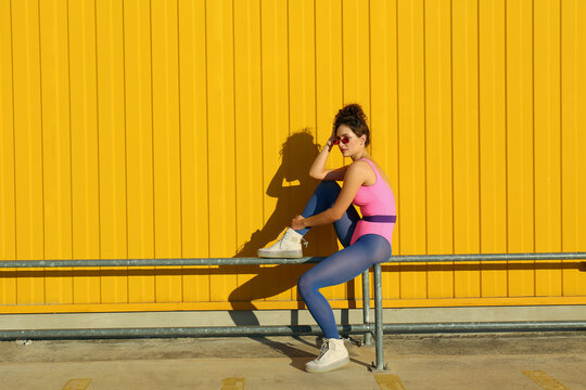 Woman sitting on railing in front of yellow wall