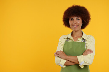 Portrait of happy young woman in apron on orange background. Space for text