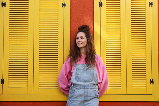 Smiling woman wearing overalls standing near wall with yellow windows