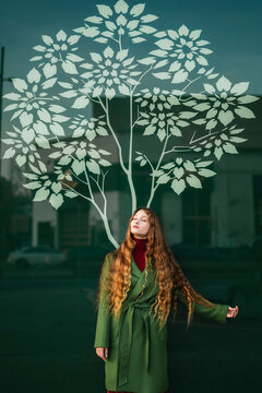 Portrait of redheaded young woman wearing green coat standing in front of glass pane with stylised tree
