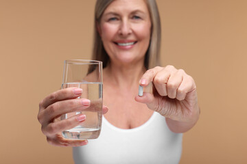 Beautiful woman with vitamin capsule and glass of water on beige background, selective focus