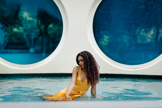 Young woman wearing yellow summer dress sitting in pool