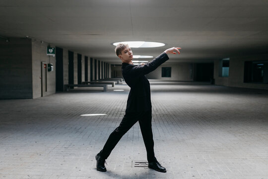 Trans young man wearing black suit dancing on floor in basement