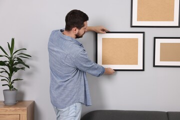 Man hanging picture frame on gray wall at home
