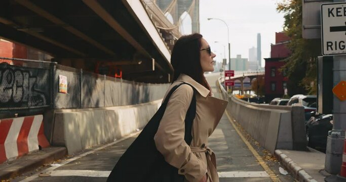 Attractive female walks around the neighborhood with the famous Brooklyn Bridge in the back in slow motion