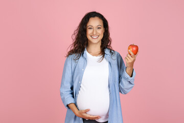 Young pregnant woman eating apple on pink background - obrazy, fototapety, plakaty
