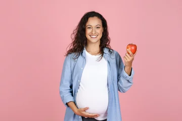 Zelfklevend Fotobehang Young pregnant woman eating apple on pink background © Prostock-studio