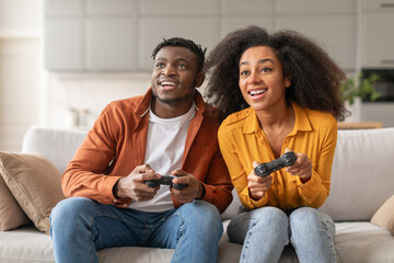 Happy black young couple playing videogames on weekend sitting indoor