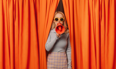 Woman talking through megaphone standing amidst orange curtains