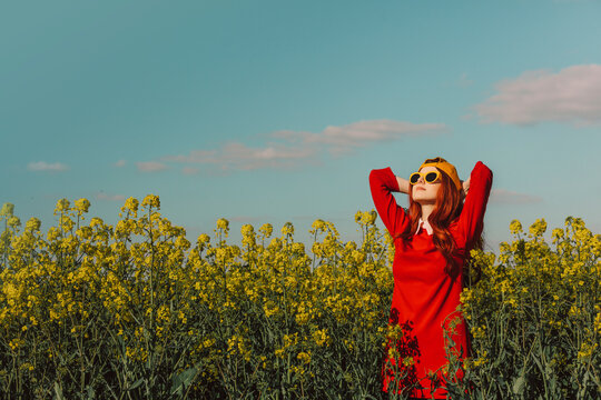 Woman with hands behind head standing in rapeseed field at sunny day