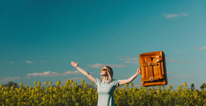 Carefree woman with suitcase standing in rapeseed field