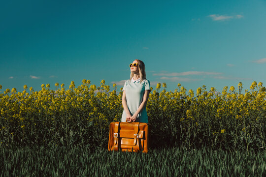 Woman with vintage suitcase standing amidst plants in rapeseed field