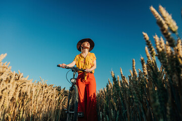 Woman standing with bicycle in wheat field