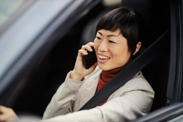 Portrait of a busy japanese businesswoman driving a car and talking on the phone.