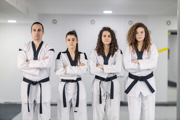 Portrait of taekwondo girls wearing kimono and black belts with their coach and looking at the camera.