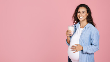 Cheerful young expecting woman holding glass of milk