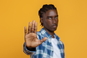 Young black man gesturing STOP with open palm on yellow studio background