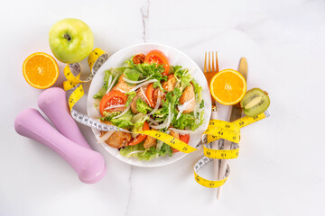Weight loss, Healthy lifestyle, diet food, sport and fitness concept. Fresh balanced vegetable and chicken breast salad with fruit, fitness equipment, dumbbell, measuring tape on a white background