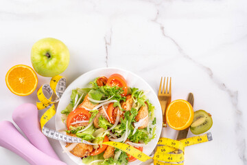 Weight loss, Healthy lifestyle, diet food, sport and fitness concept. Fresh balanced vegetable and chicken breast salad with fruit, fitness equipment, dumbbell, measuring tape on a white background